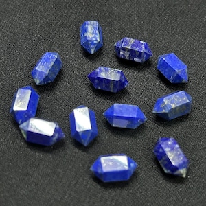 May include: A collection of faceted, deep blue lapis lazuli crystals. Each crystal has a geometric shape with multiple sides and a polished surface. Some crystals have flecks of gold-colored pyrite.
