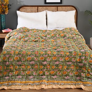 May include: A green floral quilt with orange and pink flowers on a bed with white pillows. The quilt features a repeating pattern of flowers and leaves. The bed has a woven headboard.