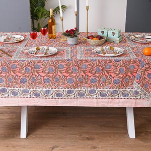 Pode incluir: Uma toalha de mesa coral com um padrão floral, pronta para uma refeição. A mesa é adornada com pratos, talheres e copos. Uma peça central de flores, frutas e velas aumenta o ambiente. A toalha de mesa mede aproximadamente 183 cm por 229 cm.