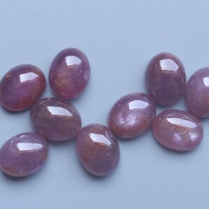 Pu&ograve; includere: Nove pietre preziose ovali e lucide in varie tonalit&agrave; di rosso-violaceo sono sparse su una superficie azzurra. Le gemme hanno una finitura liscia e lucida, che riflette la luce. Questi cabochon sono adatti per la creazione di gioielli.