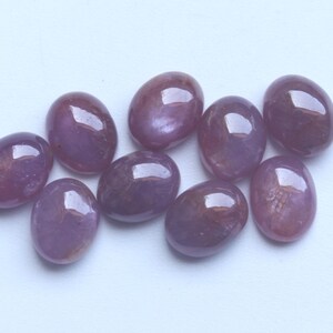 Pu&ograve; includere: Una collezione di nove pietre preziose ovali e lucide. Le pietre presentano una tonalit&agrave; viola intenso con sottili variazioni di colore e una superficie lucida e riflettente. Le pietre sono disposte su uno sfondo bianco.