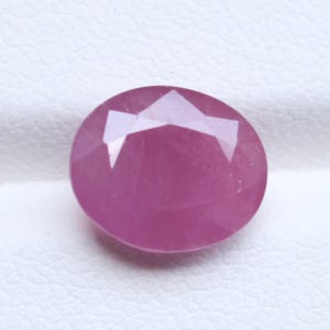 Peut inclure: Une pierre précieuse rose vif de forme ovale avec une surface à facettes. La pierre présente une qualité translucide avec de multiples coupes géométriques qui reflètent la lumière sur ses bords polis et arrondis, révélant une teinte magenta.