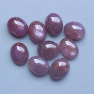 Pu&ograve; includere: Nove pietre preziose ovali e lucide in varie tonalit&agrave; di rosa e rosso sono disposte su una superficie azzurra. Le pietre preziose hanno una finitura liscia e lucida, che riflette la luce. Le pietre sembrano essere cabochon.