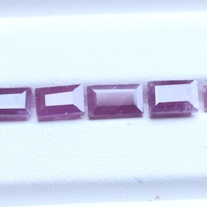 Puede incluir: Cinco piedras preciosas de color rosa-púrpura, talladas en formas rectangulares y cuadradas de diferentes tamaños. Las piedras tienen un interior más claro y están dispuestas en fila sobre una superficie blanca.