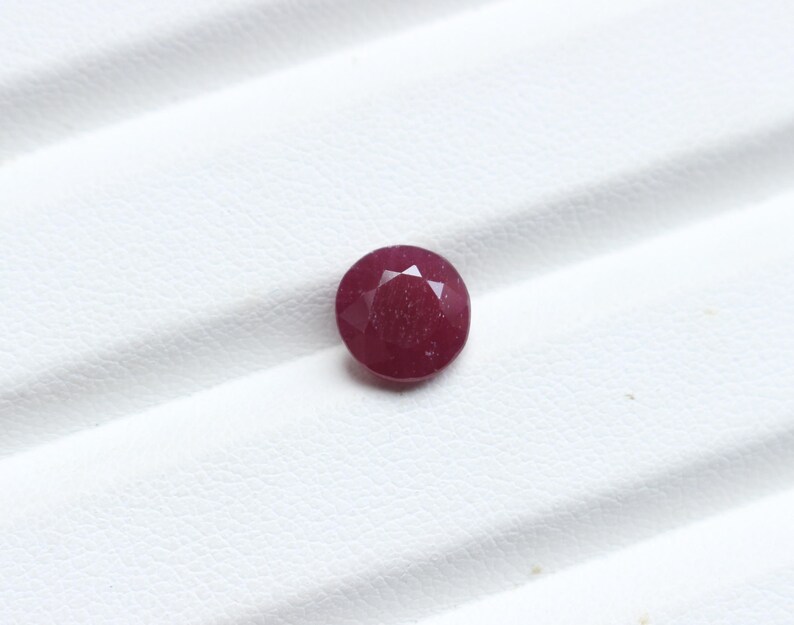 K&ouml;nnte beinhalten: Ein facettierter, runder Rubin-Edelstein. Der Edelstein hat eine tiefe, satte rote Farbe und scheint poliert zu sein. Der Rubin ist vor einem wei&szlig;en Hintergrund platziert, der seine Farbe und Form hervorhebt. Dieser Edelstein eignet sich f&uuml;r die Schmuckherstellung.