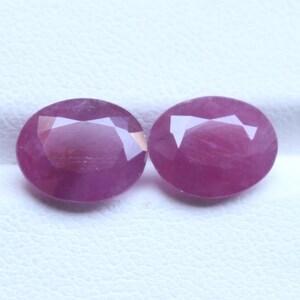May include: Two oval-cut, faceted gemstones in a deep pink colour. The gems have a polished surface with multiple facets that reflect light. The stones are set against a white background, highlighting their colour and shape. Suitable for jewellery making.
