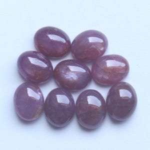 Pu&ograve; includere: Una collezione di otto pietre preziose ovali e lucide. Le pietre sono di un colore rosso-violaceo intenso con una superficie lucida e riflettente. Le pietre preziose sono disposte su uno sfondo bianco, mostrando le loro forme lisce e arrotondate. Adatto per gioielli.