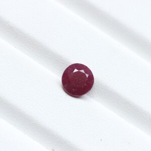K&ouml;nnte beinhalten: Ein runder, facettierter Rubin-Edelstein mit tiefroter Farbe. Der Edelstein ist vor einem wei&szlig;en Hintergrund platziert, was seine Farbe und Klarheit hervorhebt. Die Facetten des Rubins fangen das Licht ein und erzeugen einen funkelnden Effekt. Geeignet f&uuml;r die Schmuckherstellung.