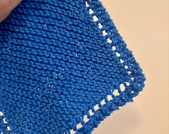 May include: Close-up of a knitted square in a bright blue shade. The square has a textured stitch pattern and an openwork border. The item is held by a hand, highlighting the texture and colour.