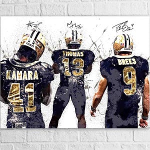 May include: Artwork featuring three football players in black and gold uniforms. The players are wearing helmets and jerseys with the names Kamara, Thomas, and Brees, and numbers 41, 13, and 9. The background has white paint splatters.