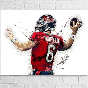 May include: An artistic rendering of a football player in a red jersey with the name "MAYFIELD" and the number "6". The player is wearing a black helmet with a skull logo and is throwing a football. The background has paint splatter effects.