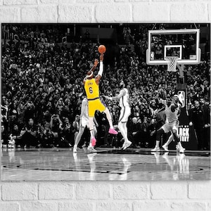 May include: Black and white basketball action shot with a player in a yellow jersey, number 6, shooting a basketball. Other players in white jerseys are jumping. The background is a crowd of people.