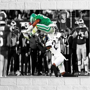 May include: A dynamic action shot of a football player in a green and white uniform leaping over a player in a white and black uniform. The background is a black and white crowd with a number 3 sign.