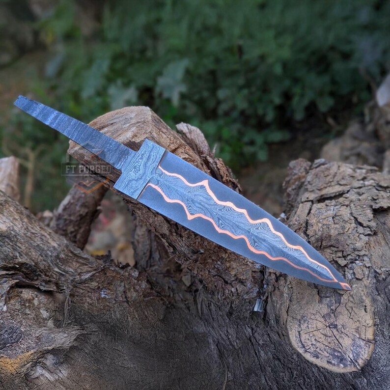A horizontal view of a Damascus steel knife blank resting on a textured wooden stump outdoors.