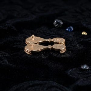 May include: A pair of gold-toned drop earrings featuring a teardrop-shaped top section connected to a circular bottom piece. The back of each earring displays a textured, patterned surface with a post and clutch closure, and the metal is stamped 925.