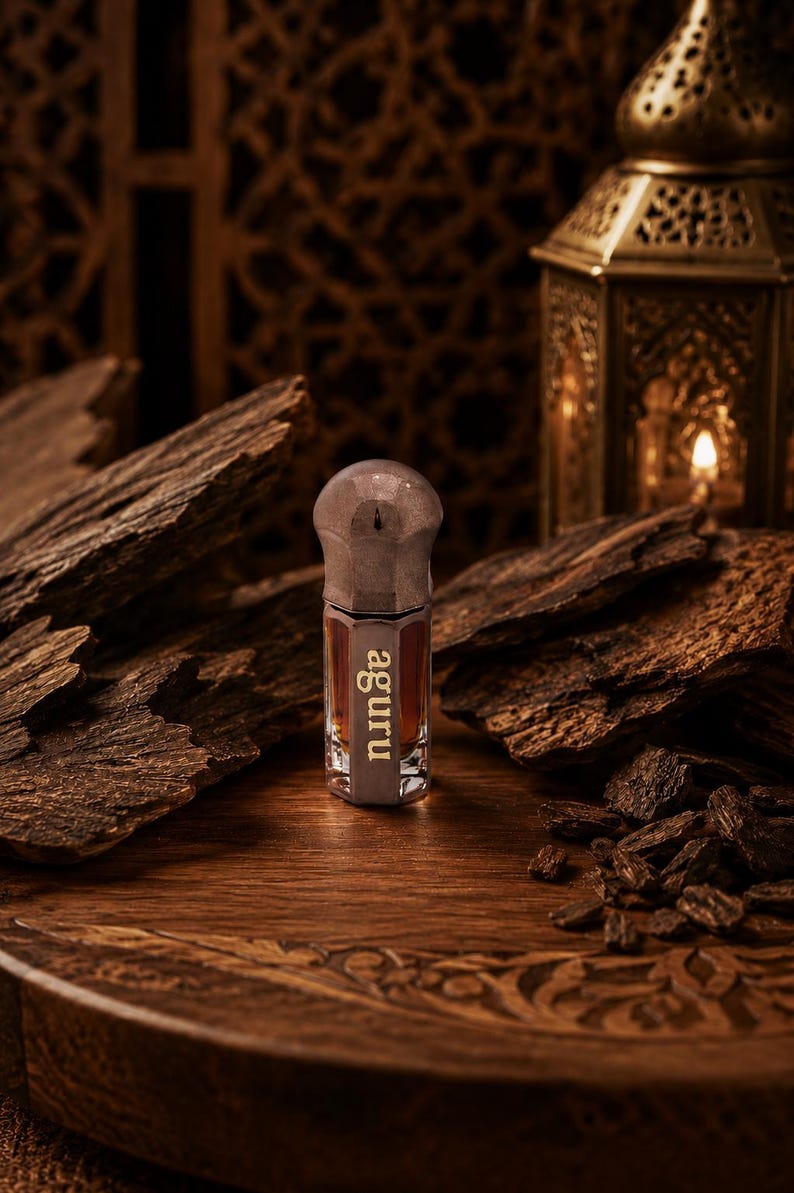 May include: A small, hexagonal glass bottle filled with a dark amber liquid, featuring a metallic cap and the word "aguru" printed in white on the front. The bottle stands upright, showcasing its clear glass construction and distinct shape.