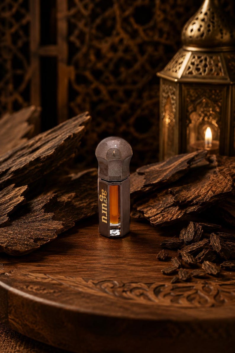 May include: A small, hexagonal glass bottle containing amber-colored liquid, featuring a metallic cap and the word "aguru" printed vertically in white on the side. The bottle has a clear glass body and a smooth, rounded metallic top.