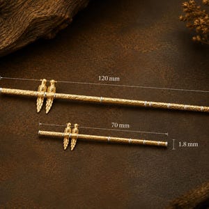 Puede incluir: Dos horquillas de metal dorado con superficie texturizada y un par de figuras de aves. La m&aacute;s larga mide 120 mm de largo y 2,8 mm de di&aacute;metro, mientras que la m&aacute;s corta mide 70 mm de largo y 1,8 mm de di&aacute;metro.