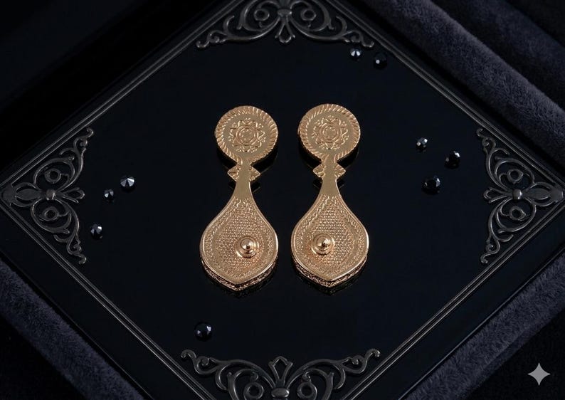 May include: A pair of gold-toned drop earrings featuring a circular top section with an intricate embossed pattern and a larger, teardrop-shaped bottom section with a textured, mesh-like surface and a small central stud detail on each piece.