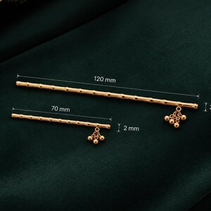 Puede incluir: Dos horquillas doradas con un dise&ntilde;o texturizado similar al bamb&uacute;. La varilla m&aacute;s larga mide 120 mm de largo y 2,5 mm de di&aacute;metro, mientras que la m&aacute;s corta mide 70 mm de largo y 2 mm de di&aacute;metro. Ambas tienen peque&ntilde;as cuentas doradas colgantes.