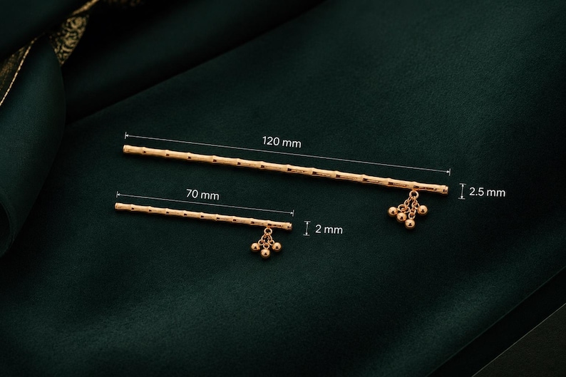 Puede incluir: Dos horquillas doradas con un dise&ntilde;o texturizado similar al bamb&uacute;. La varilla m&aacute;s larga mide 120 mm de largo y 2,5 mm de di&aacute;metro, mientras que la m&aacute;s corta mide 70 mm de largo y 2 mm de di&aacute;metro. Ambas tienen peque&ntilde;as cuentas doradas colgantes.
