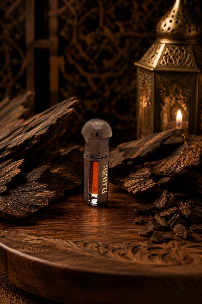 May include: A small, hexagonal glass bottle containing a dark amber liquid, featuring a metallic cap and the word aguru printed vertically on the side. The bottle is surrounded by several pieces of dark, textured wood chips on a wooden surface.