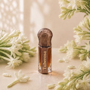 May include: A small, hexagonal glass perfume bottle filled with amber-colored liquid. The bottle features a dark, metallic, rounded cap and the word Tuberosa printed vertically in white lettering on the front face of the glass container.