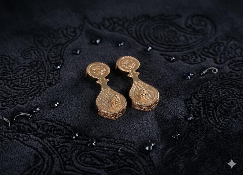May include: A pair of gold-toned drop earrings featuring a circular top section connected to a larger, teardrop-shaped base. Both components are decorated with intricate, embossed patterns and a central stud detail on the lower portion.
