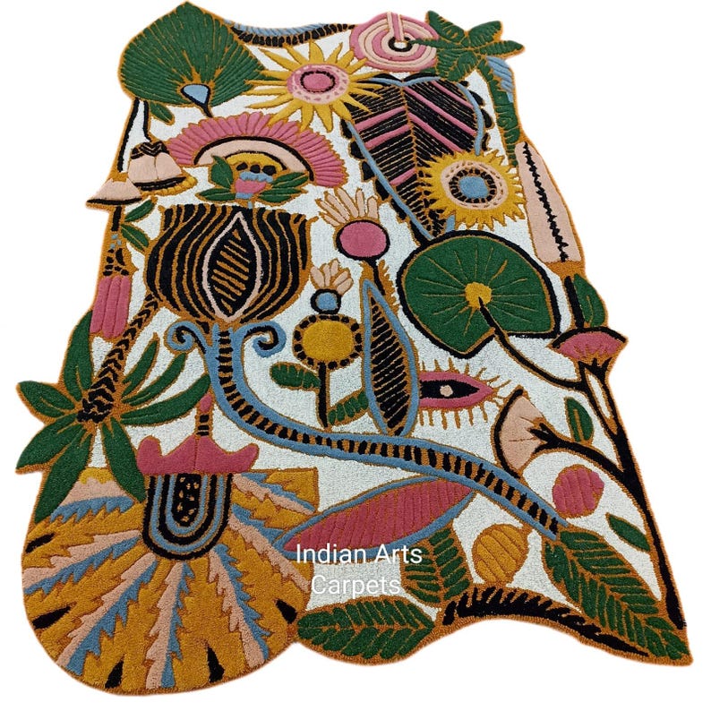 May include: A colorful, floral-patterned rug with a white background. The rug features a variety of flowers and leaves in shades of green, pink, yellow, and blue. The text "Indian Arts Carpets" is visible on the rug.