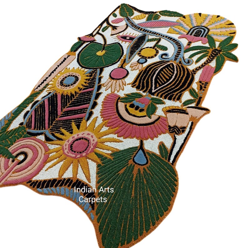 May include: A colorful, floral-patterned rug with a white background. The rug features large, stylized flowers in shades of pink, yellow, and green, with black and blue accents. The text "Indian Arts Carpets" is visible on the rug.