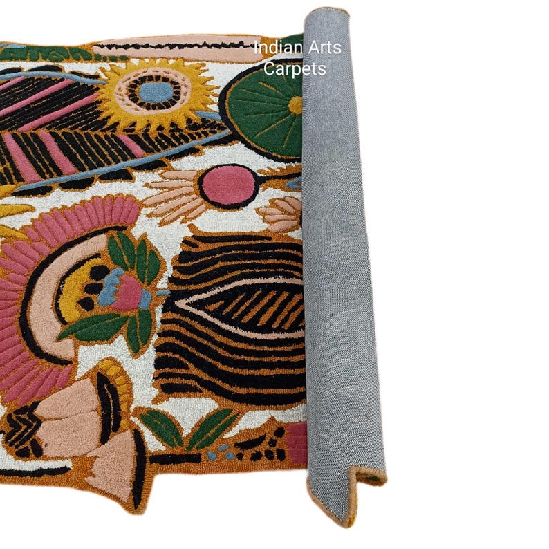 May include: A rolled-up, colorful rug with a floral design. The rug features pink, yellow, green, and black patterns on a white background. The text "Indian Arts Carpets" is visible on the rug.