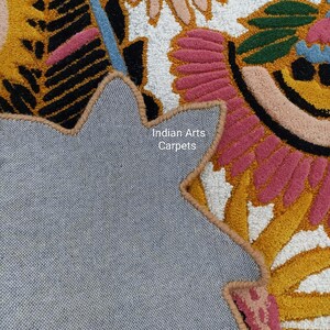 May include: Close-up of a colorful floral rug with a gray backing. The rug features a vibrant design with pink, yellow, black, and blue accents. The text "Indian Arts Carpets" is visible on the backing.