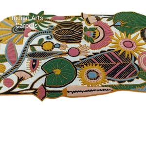 May include: A colorful, floral-patterned rug with a white background. The rug features various flowers and leaves in shades of pink, yellow, green, and black. The text "Indian Arts Carpets" is visible in the upper left corner.