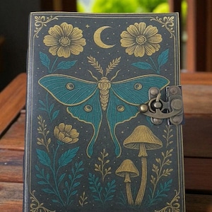 Peut inclure: Un journal bleu canard foncé avec un motif détaillé représentant un grand papillon de nuit bleu sarcelle, des fleurs, des champignons et un croissant de lune. La couverture a une bordure décorative et une fermeture à fermoir en métal.