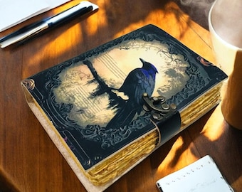 Può includere: Un diario rilegato in pelle con un'illustrazione di un corvo sulla copertina. Il corvo blu scuro e nero è appollaiato su un ramo su uno sfondo attenuato. Il diario è assicurato con un cinturino in pelle nera e una chiusura in metallo.