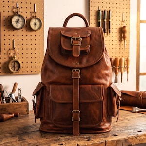 May include: A brown leather backpack featuring a top handle, a flap closure with a buckle, a small front pocket with a buckle, two side pockets, and a large lower front pocket secured by a vertical strap with two buckles, all with antique brass hardware.