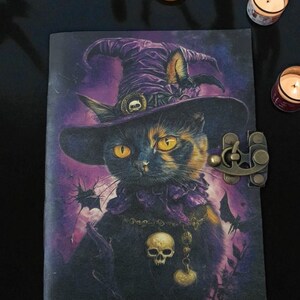 以下が含まれることがあります： 魔女の帽子をかぶった黒猫が描かれた日記帳。スカルペンダントと装飾的な留め金が付いています。猫は黄色い目を持ち、コウモリのいる紫色の背景に配置されています。ユニークなゴシックテーマの日記帳です。