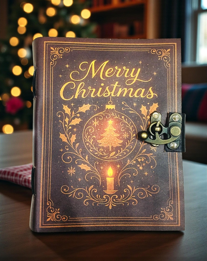 May include: A brown journal with the words "Merry Christmas" in gold script. The cover features a gold illustration of a Christmas tree, ornaments, and a candle. The journal has a metal clasp and is on a wooden surface.