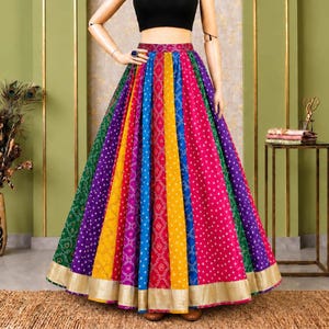 Op de afbeelding: Een zwarte mouwloze crop top gecombineerd met een vloerlange, veelkleurige geplooide rok met verticale panelen van groene, paarse, gele, blauwe en roze stof met een wit stippenpatroon en een brede metallic gouden rand aan de zoom.