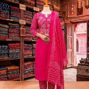Puede incluir: Un conjunto de tres piezas en color rosa brillante que consta de una túnica de manga larga con cuello hendido, pantalones rectos a juego y una dupatta coordinada, todo con un patrón de teñido anudado blanco con motivos geométricos y de puntos.