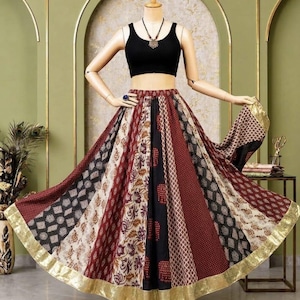 May include: A black sleeveless crop top paired with a long, flared skirt featuring vertical panels of maroon, black, and cream fabric with various geometric and floral patterns. The skirt is finished with a wide, metallic gold border at the hem.