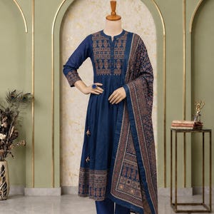 May include: A dark blue three-piece outfit consisting of a long-sleeved kurta with a mandarin collar, matching trousers, and a coordinating dupatta. The kurta features a copper-colored geometric and paisley print on the chest and hem.