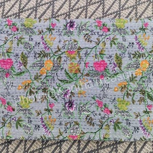 May include: A rectangular, floral-patterned quilt with a light gray background. The quilt features a repeating pattern of pink, orange, purple, and green flowers and leaves. The quilt is hand-stitched with white thread.