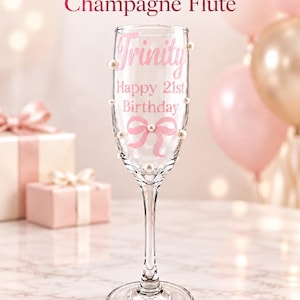 May include: A clear glass champagne flute decorated with small white pearls and a pink bow graphic. The glass features the text Trinity, Happy 21st Birthday in pink lettering. The top of the image displays Personalized Birthday Champagne Flute.