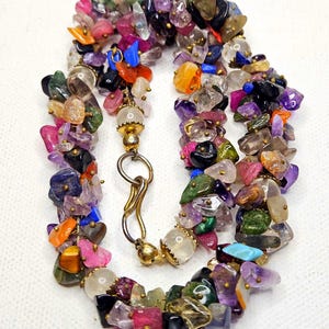 May include: A colorful necklace composed of various small, irregularly shaped gemstones in shades of pink, purple, orange, green, and blue. The stones are strung together with gold-colored metal accents and a clasp.