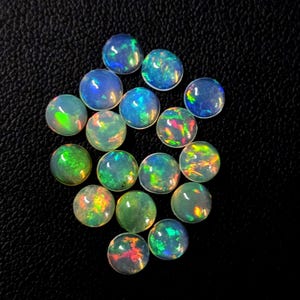 May include: A collection of round opals with a polished, iridescent surface. The opals display a range of colors, including blue, green, and orange, and are set against a black background.