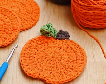 May include: Handmade orange crochet pumpkins with green and brown detailing, ideal for autumn decorations. The image also shows a blue crochet hook and orange yarn, suggesting a craft project. The pumpkins are round and have a textured appearance.