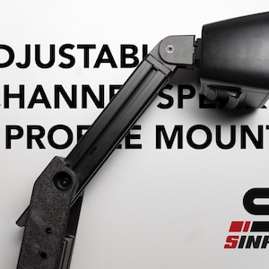 May include: Black adjustable channel speaker profile mount. The mount is angled and has a black speaker attached. The text "ADJUSTABLE CHANNEL SPEAKER PROFILE MOUNT" is printed in black. The logo "SINHRIG" is in red and black.