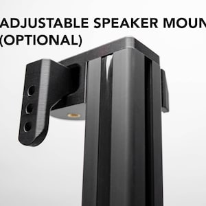 Puede incluir: Soporte de altavoz ajustable negro con el texto "ADJUSTABLE SPEAKER MOUNT (OPTIONAL)". El soporte tiene un diseño rectangular con un soporte y tres agujeros circulares. El texto es en negro y rojo.