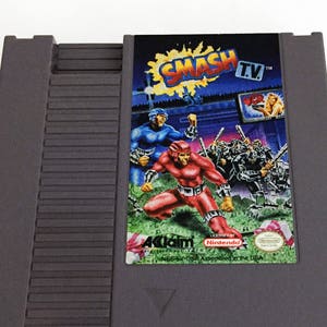 May include: A gray Nintendo Entertainment System (NES) game cartridge for the game "Smash TV". The game cartridge features a colorful image of the game's characters and a red and white "Acclaim" logo.